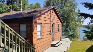 A wooden cabin with a deck, a window, and a door.