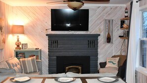 A cozy living room with a fireplace, a mounted TV, and a dining area with plates set.