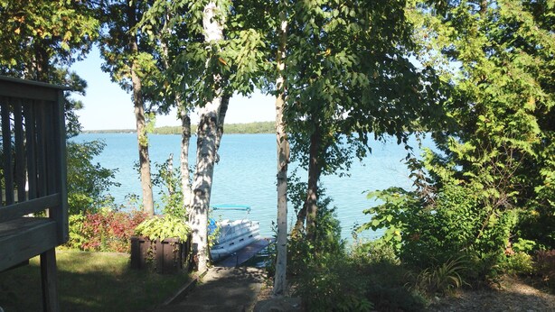 A wooden deck leading to a dock by a calm lake, surrounded by trees and greenery.