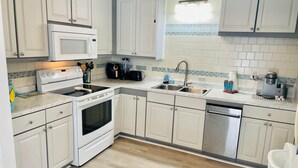 A modern kitchen with white cabinets, a stainless steel sink, a microwave, a stove, and a dishwasher.