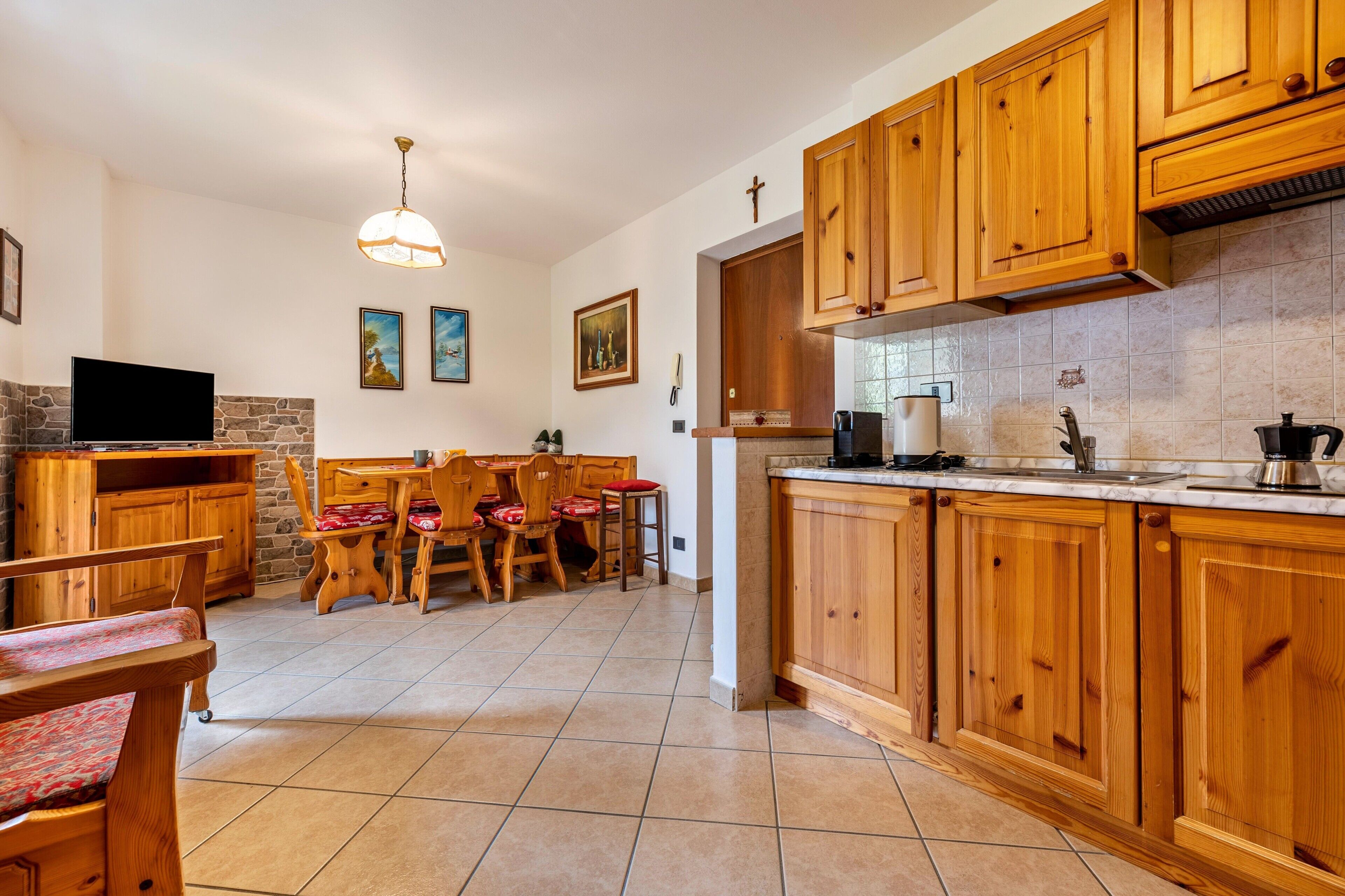 Une cuisine avec des meubles en bois, une table à manger avec des chaises, un téléviseur et un mur en pierre.