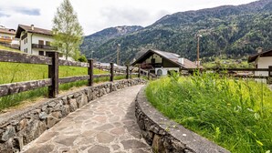A stone pathway leading to a rustic building with a wooden fence and a mountain backdrop. - Apartment 'Collini Le Betulle' with Mountain View, Private Garden and Balcony (Spiazzo)