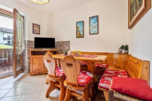 A dining area with wooden chairs and benches, a stone fireplace, and a television on a wooden cabinet. - Apartment 'Collini Le Betulle' with Mountain View, Private Garden and Balcony (Spiazzo)