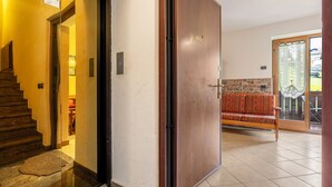 A hotel entrance with a wooden door, a staircase, a red patterned sofa, and a stone wall. - Apartment 'Collini Le Betulle' with Mountain View, Private Garden and Balcony (Spiazzo)