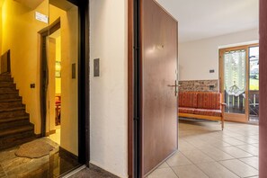 Entrada de hotel con puerta de madera, una escalera, un sofá rojo con estampado y una pared de piedra.