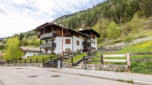 A two-story chalet with a balcony, stone steps, and a wooden fence. - Apartment 'Collini Le Betulle' with Mountain View, Private Garden and Balcony (Spiazzo)