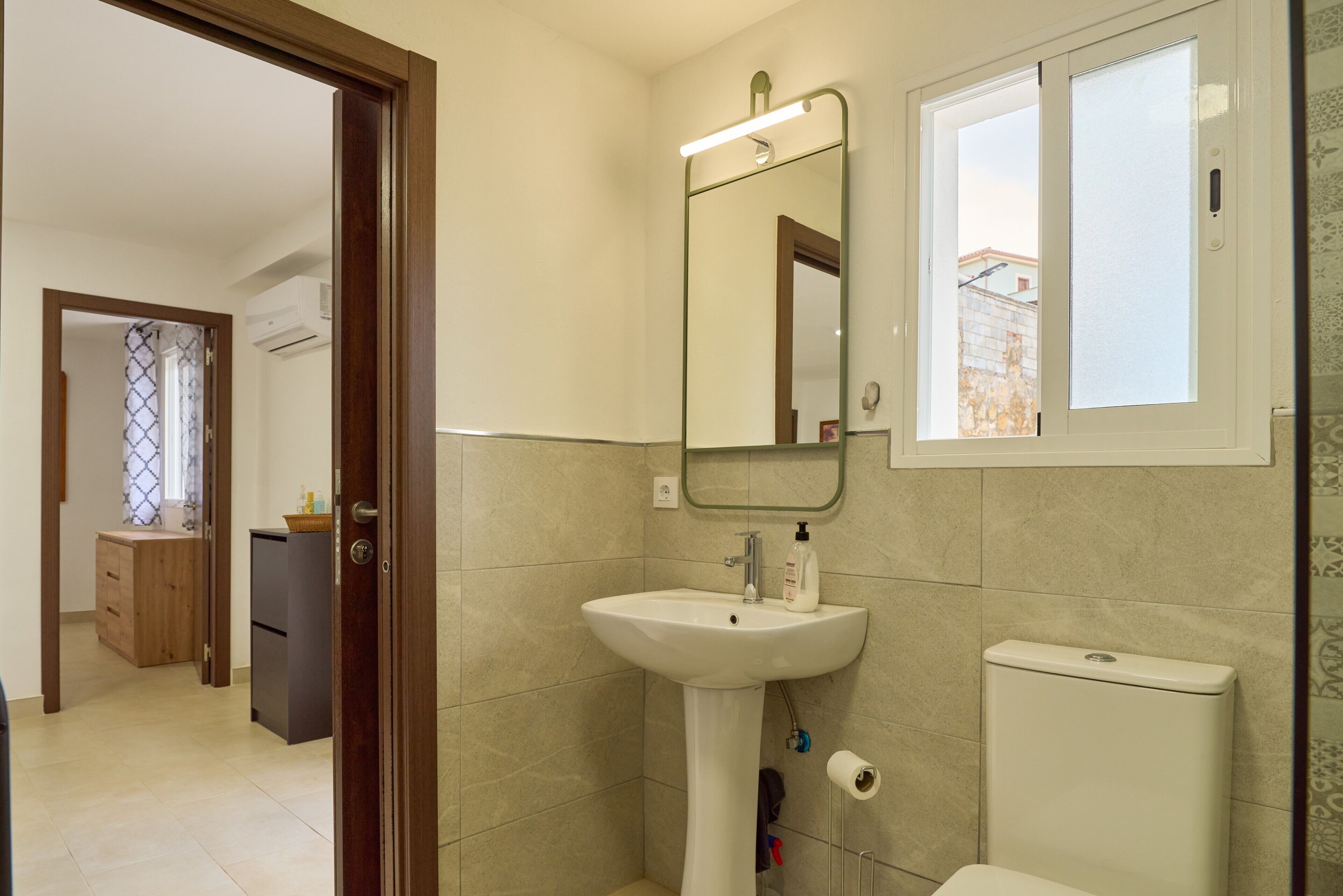 Un baño con lavamanos, espejo, inodoro y ventana.