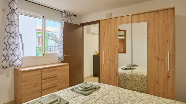Camera da letto con un letto, un armadio in legno, una finestra con tende a motivi e vista sugli edifici esterni.