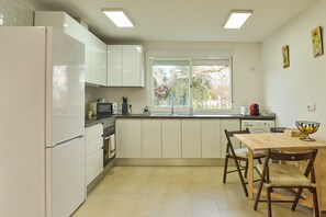 A modern kitchen with white cabinets, a built-in oven, a microwave, and a dining area with wooden chairs and a table. - Holiday Home 'Villa Verde' with Shared Pool, Wi-Fi and Air Conditioning (Córdoba)