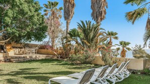 A row of white lounge chairs on a grassy lawn, surrounded by palm trees and a stone wall. - Apartment 'Villa Colliure' with Sea View, Private Pool and Wi-Fi (Adeje)