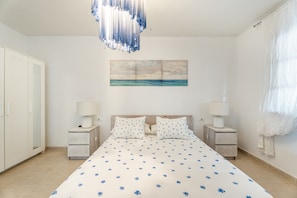 A bedroom with a bed, two bedside tables, a hanging light fixture, a painting on the wall, and a door. - Villa 'Cassis' with Sea View, Private Pool and Wi-Fi (Adeje)