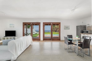 A modern hotel room with a bed, TV, dining table, chairs, and a view of the ocean through glass doors. - Villa 'Cassis' with Sea View, Private Pool and Wi-Fi (Adeje)