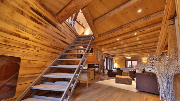 A wooden interior with a staircase, seating area, and a kitchen.