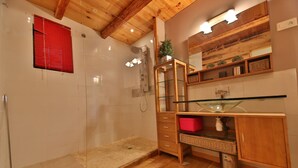 A modern bathroom with a glass shower enclosure, wooden vanity, and a red storage bin.