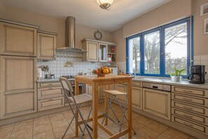 A kitchen with a wooden table, a chair, a sink, cabinets, and a window with a view. - Holiday Home 'Maison 6 Pers 100m Plage' with Sea View, Private Terrace and Wi-Fi (TREGUNC)