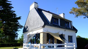 Uma casa de dois andares com fachada branca, telhado escuro e varanda com área de estar externa.