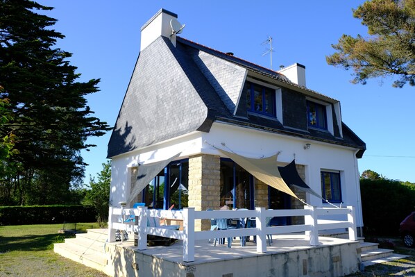 A two-story house with a white exterior, a dark roof, and a balcony with outdoor seating.