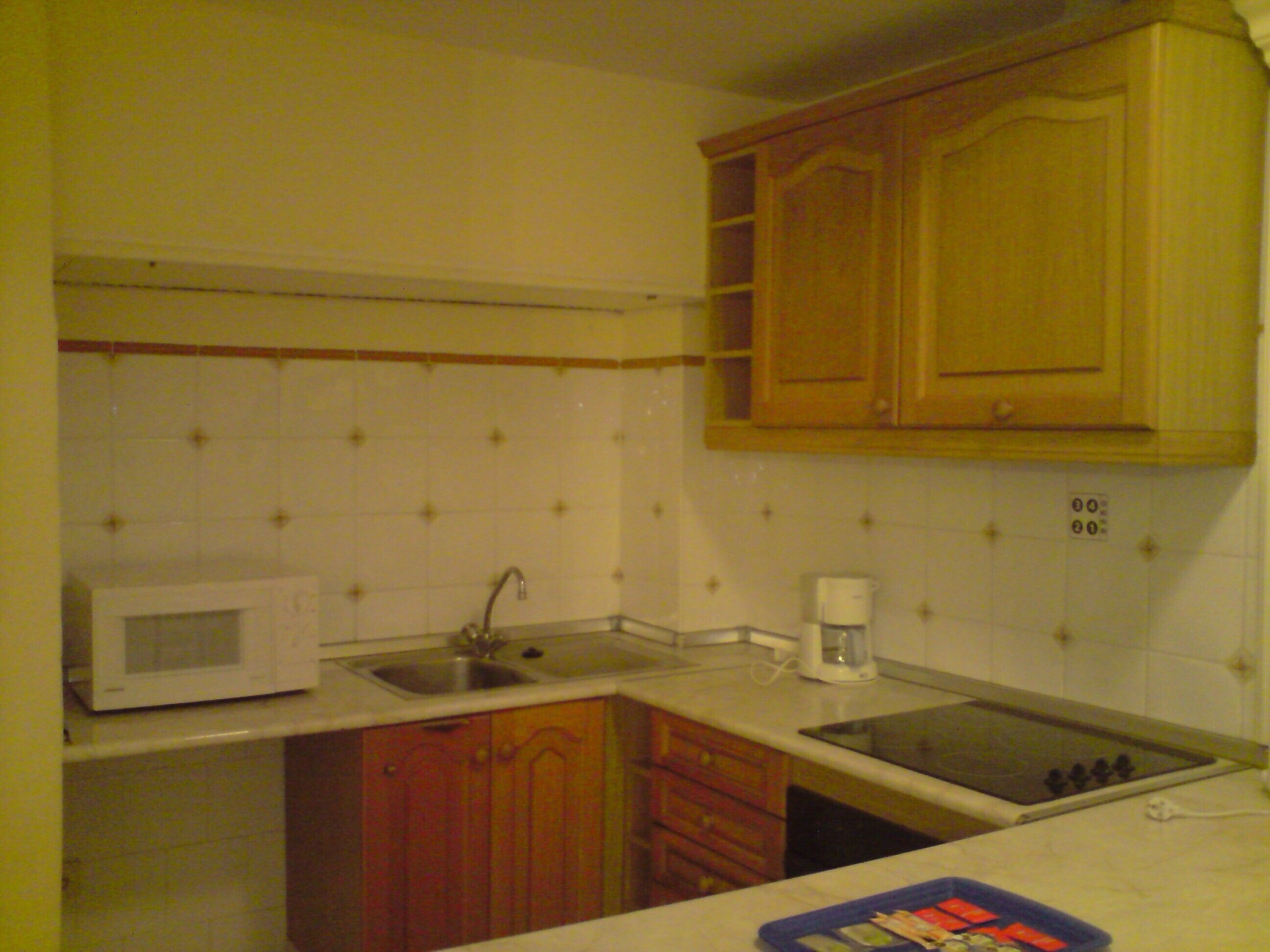 A kitchen with white tiles, wooden cabinets, a microwave, a sink, and a stove.