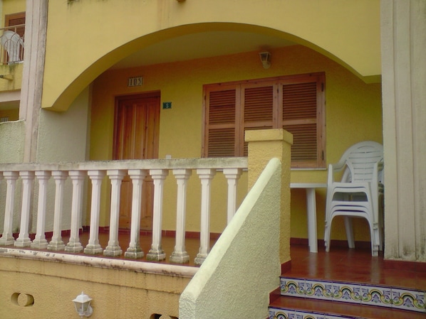 A building with a yellow facade, a balcony with white balustrades, and a staircase leading to a door marked '103'.