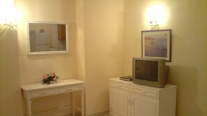 Un baño con tocador, espejo, armario y televisor sobre un soporte.