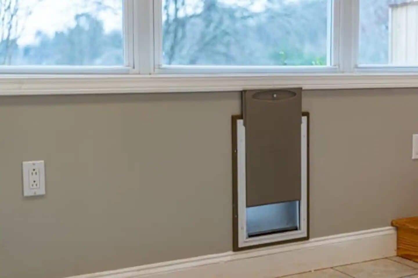 A room with a window, a wall-mounted electrical outlet, and a door frame.