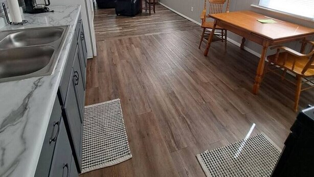 A modern kitchen with a marble countertop, wooden flooring, and a dining area with a wooden table and chairs. - Charming Magnolia Apartment (Magnolia)