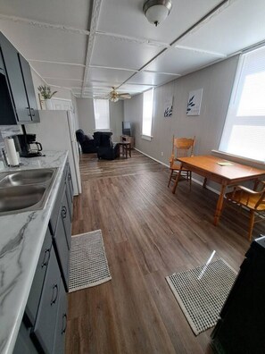 A modern kitchen with a marble countertop, wooden flooring, and a dining area with a wooden table and chairs.