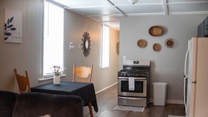 A modern kitchen with a stove, oven, and refrigerator. There is a dining table with chairs and a window with blinds. - Charming Magnolia Apartment (Magnolia)