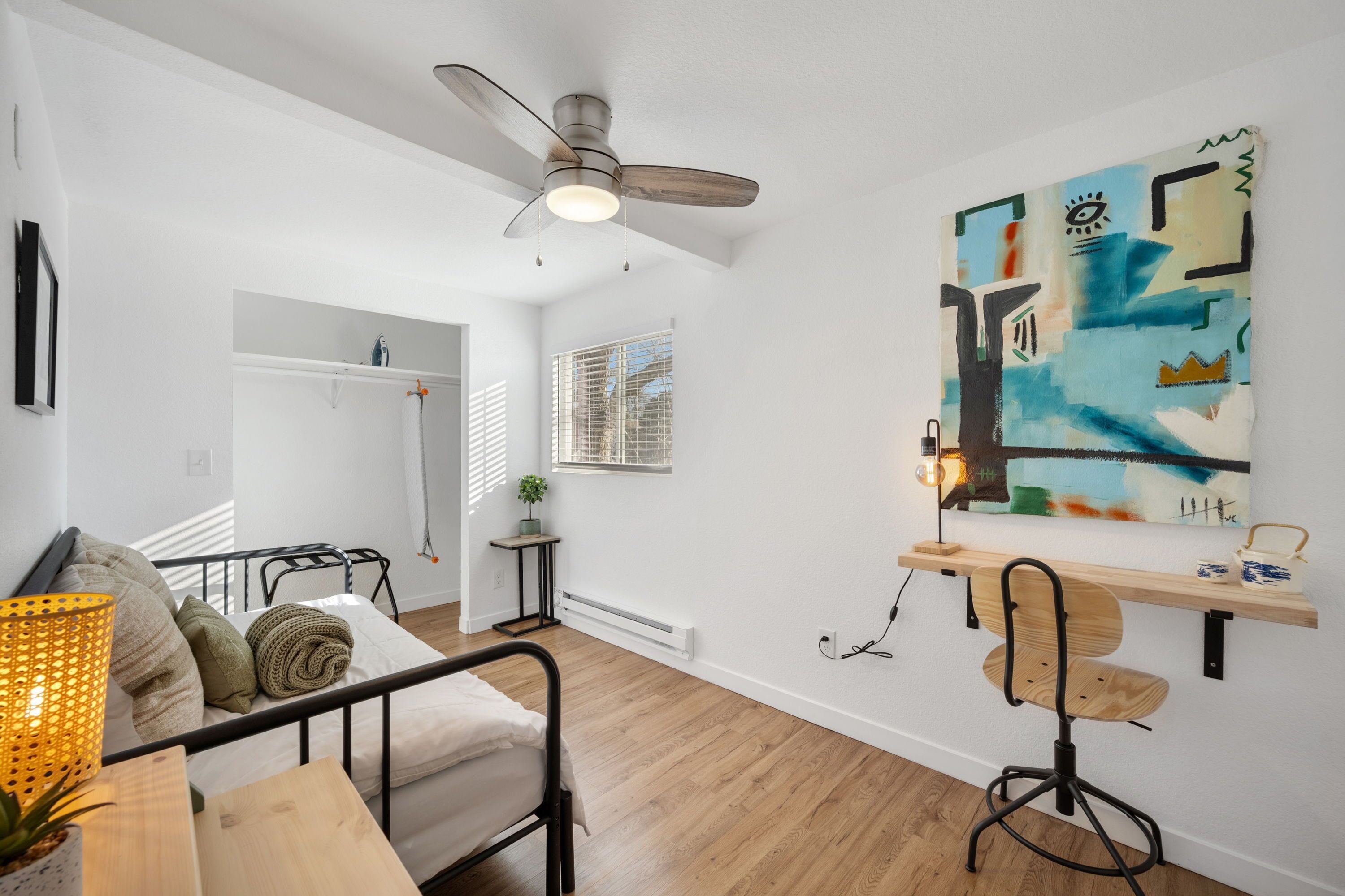 A modern living room with a ceiling fan, a dining table, a sofa, and a painting on the wall.