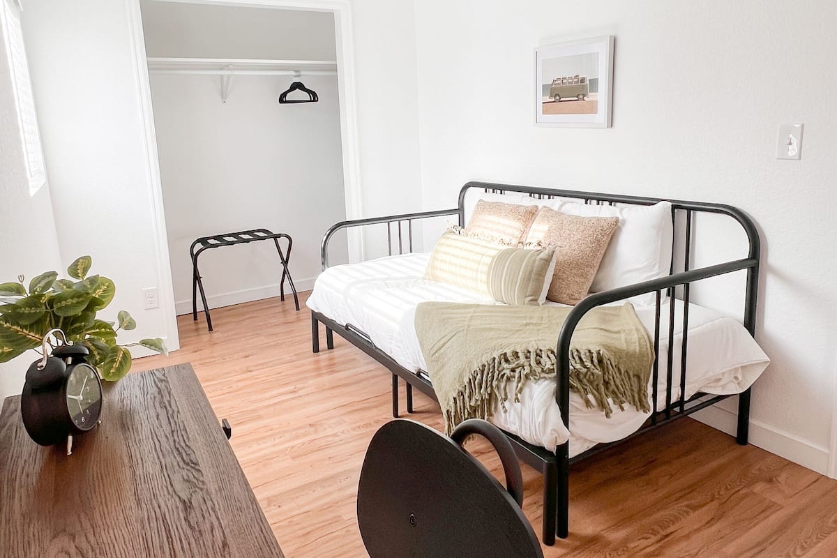 Een slaapkamer met een bed, een plafondventilator, een nachtkastje, een stoel en een plant.
