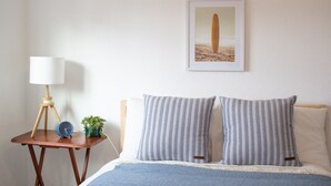 Une chambre à coucher bien rangée, avec un lit, des oreillers, une table de chevet avec une lampe, une horloge et une petite plante.