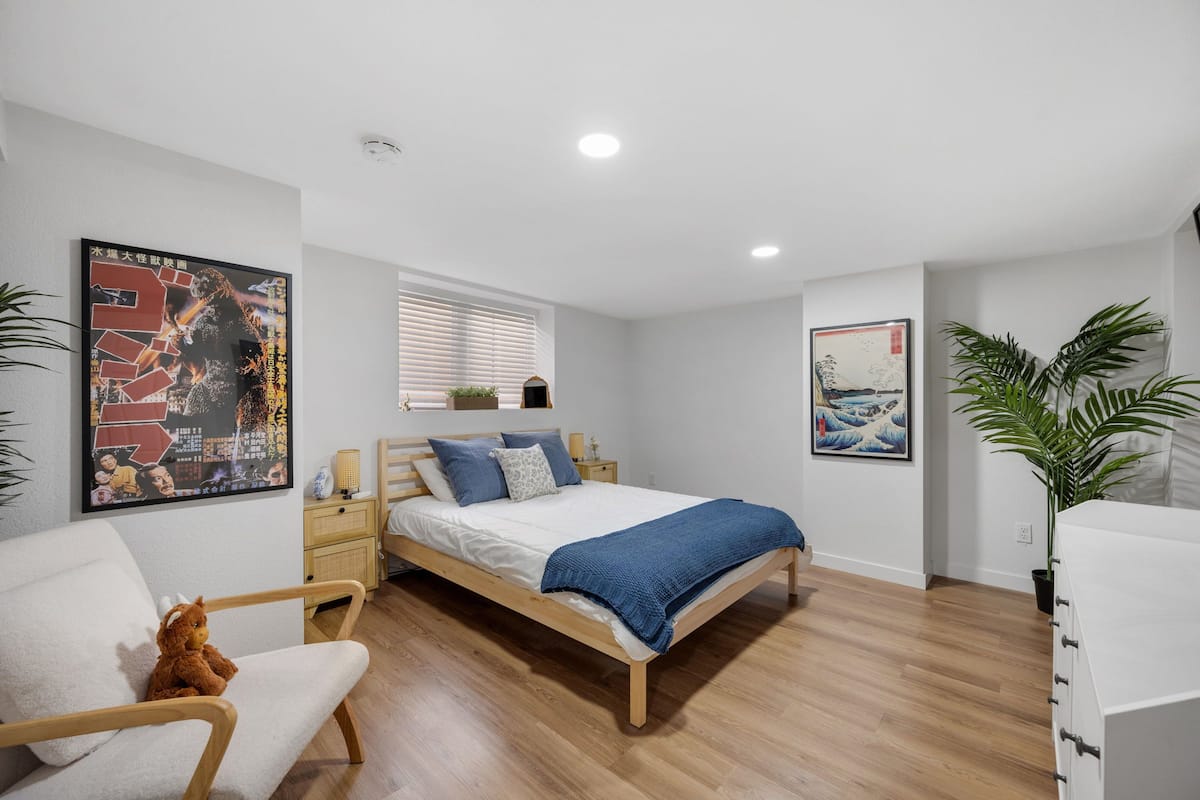Een slaapkamer met een houten bed, witte muren en een groot poster aan de linkerkant.