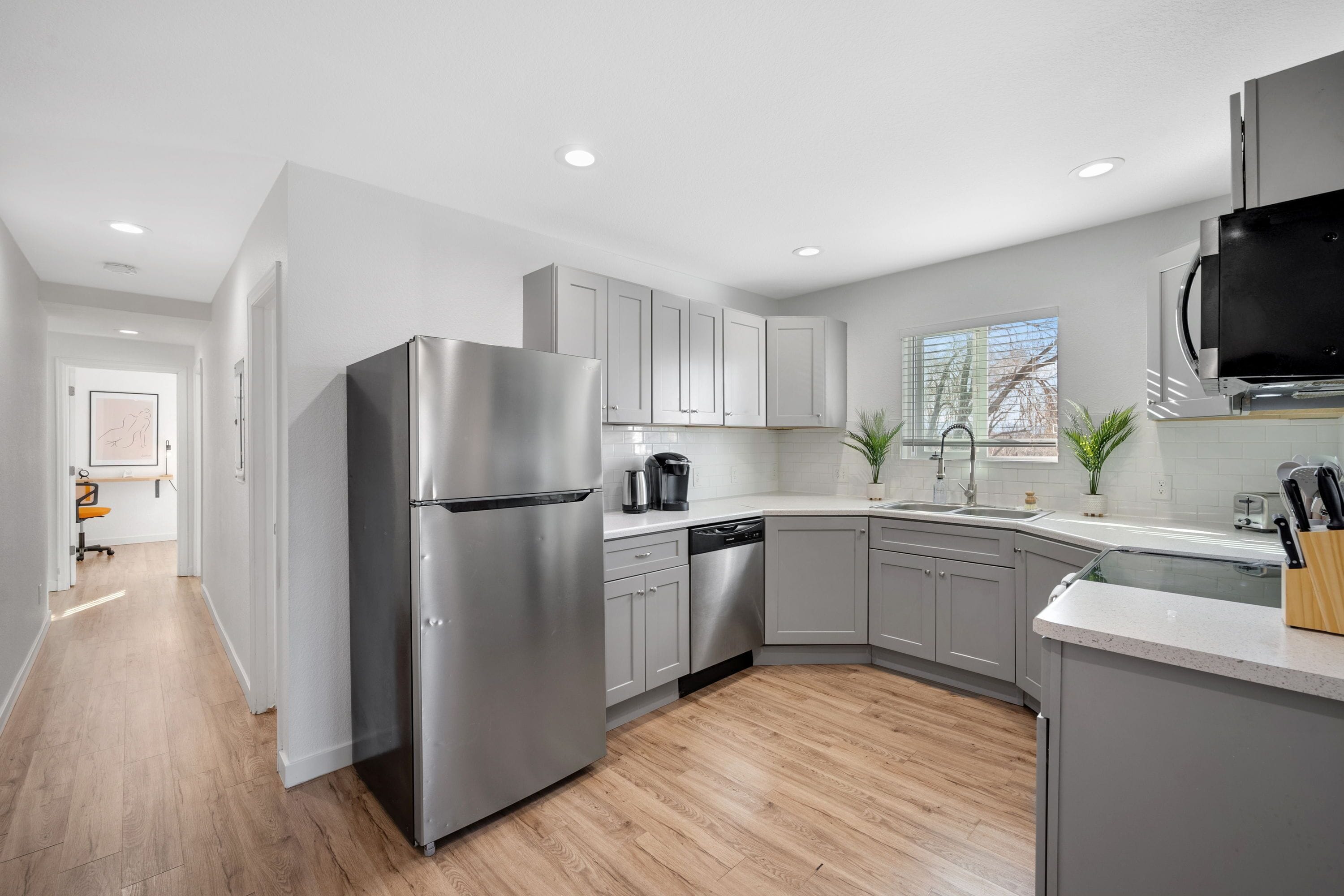 A modern kitchen with stainless steel appliances, grey cabinets, and a wooden floor.