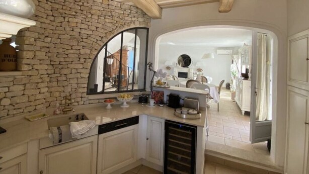 A kitchen with a stone wall, wooden beams, a large mirror, and a view into the dining area. - Maison sur la Colline, Lagnes Proche de Gordes et Lisle sur la Sorgue (Lagnes)