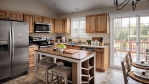 Une cuisine moderne avec des meubles en bois, des appareils électroménagers en acier inoxydable et une grande fenêtre donnant sur une terrasse.