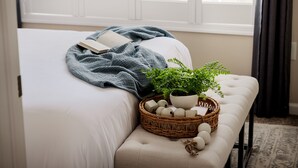 Un lit bien fait, recouvert d’une couverture bleue, avec un livre, une plante en pot et un panier en osier contenant des œufs et une décoration en forme d’étoile.