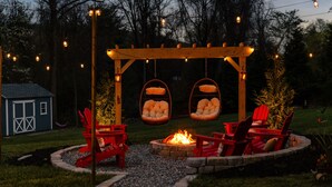 Une pergola en bois agrémentée de fauteuils suspendus et d’un foyer, le tout installé dans un jardin.