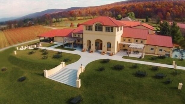 Un grand bâtiment à deux étages, avec un toit rouge, entouré d’une pelouse bien entretenue et d’un vignoble en arrière-plan.