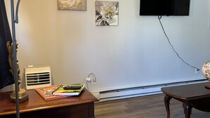 Un salon avec un téléviseur à écran plat fixé au mur, une table basse en bois, un fauteuil rembourré et un lampadaire.