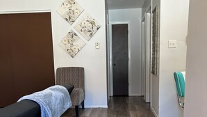 Une pièce avec un plancher en bois, une table de massage noire, une chaise à rayures et une chaise de couleur turquoise.