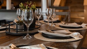 Una mesa de comedor de madera dispuesta con platos, vasos y cubiertos, y un florero con flores en el centro.