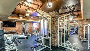 A gym with various exercise equipment, a stone wall, and a television screen. - Westgate 8th Floor Remodeled Luxury Studio Suite- Ski-In/Out, Full Kitchen (Park City)