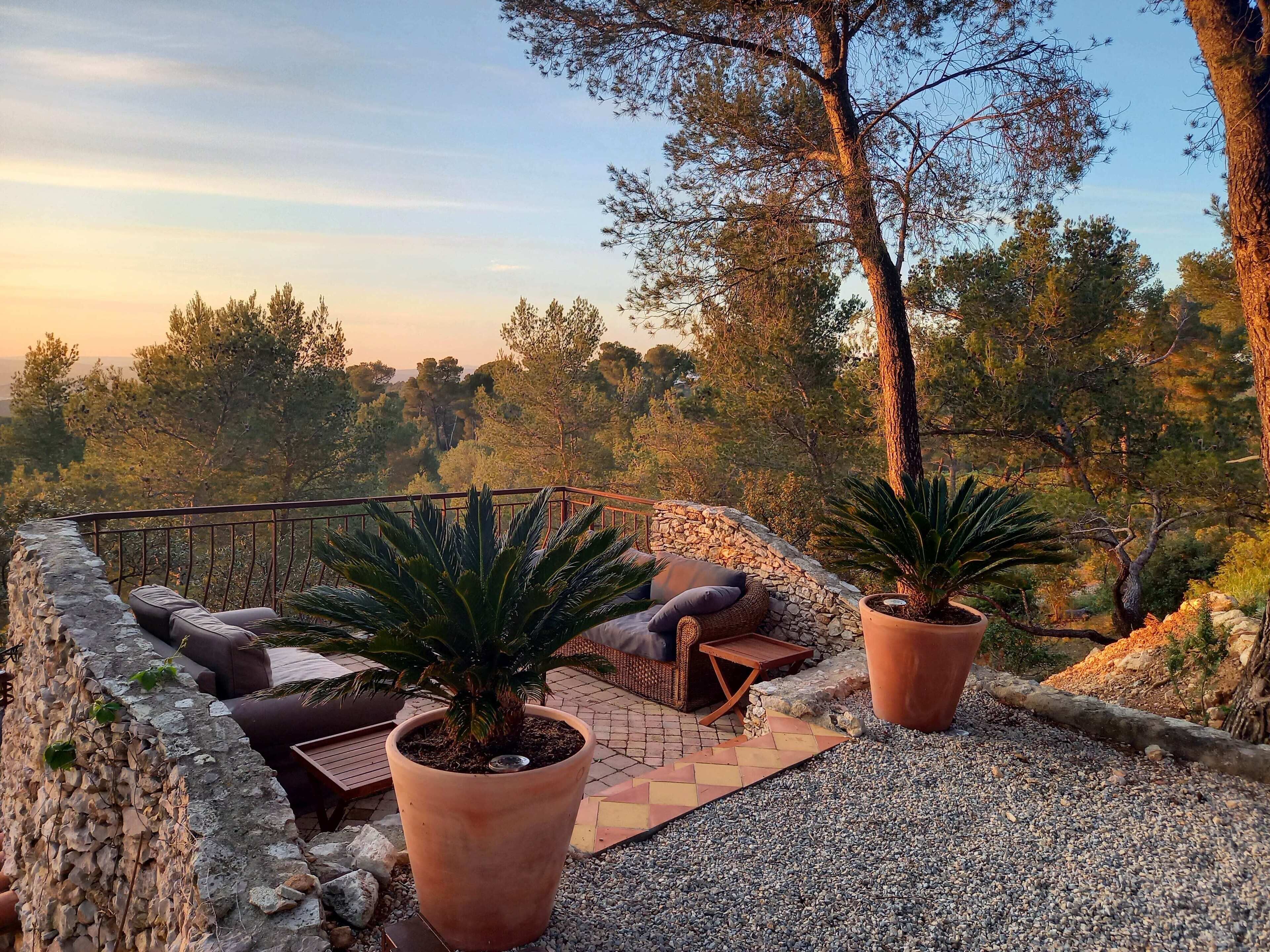 A terrace with stone walls, potted plants, outdoor furniture, and a view of a forested landscape.