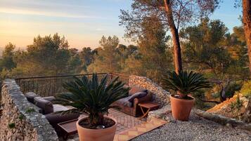 A terrace with stone walls, potted plants, outdoor furniture, and a view of a forested landscape.