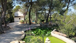 A serene garden with a pond, surrounded by trees and a white building with a tiled roof. - Le Moulin Rouge Provençal : charming old windmill with hot tub close to Aix (Bouc-Bel-Air)