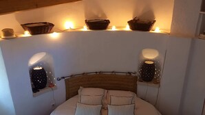 Een slaapkamer met een groot bed, twee wandlampen en een plank met manden.