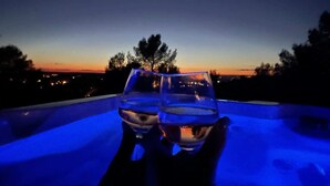 Een nachtscène met twee glaasjes water op een balkon, met uitzicht op een stadsbeeld bij zonsondergang.