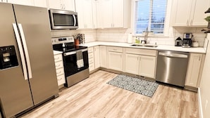 A modern kitchen with white cabinets, stainless steel appliances, and a wooden floor. - Beautiful, newly built 4 bedroom with garage (Yakima)