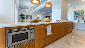 A modern kitchen with a built-in oven, wooden cabinets, and a large island with a sink. - Renovated Beachfront 3 BR - Steps to Baha Mar (Nassau)