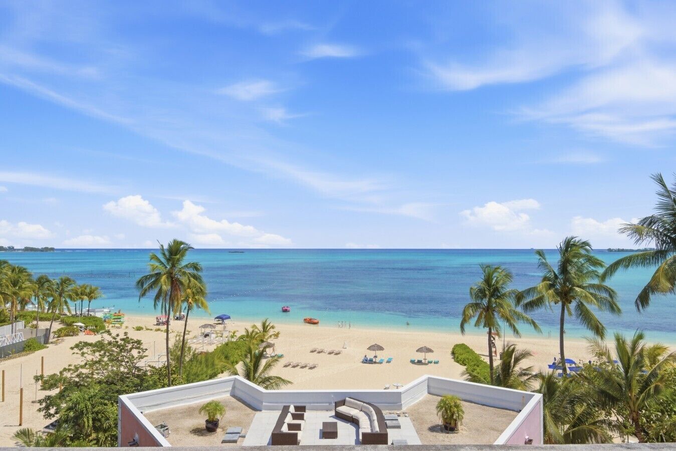 A beach view with palm trees, a pool area, and a clear sky.